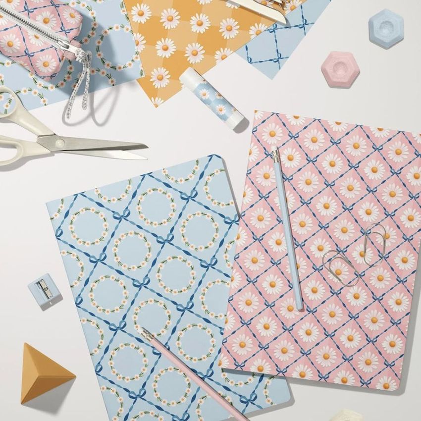 Stationery mockup featuring two classic A4 notebooks with pastel daisy and bow patterns, surrounded by office supplies on a light surface.
