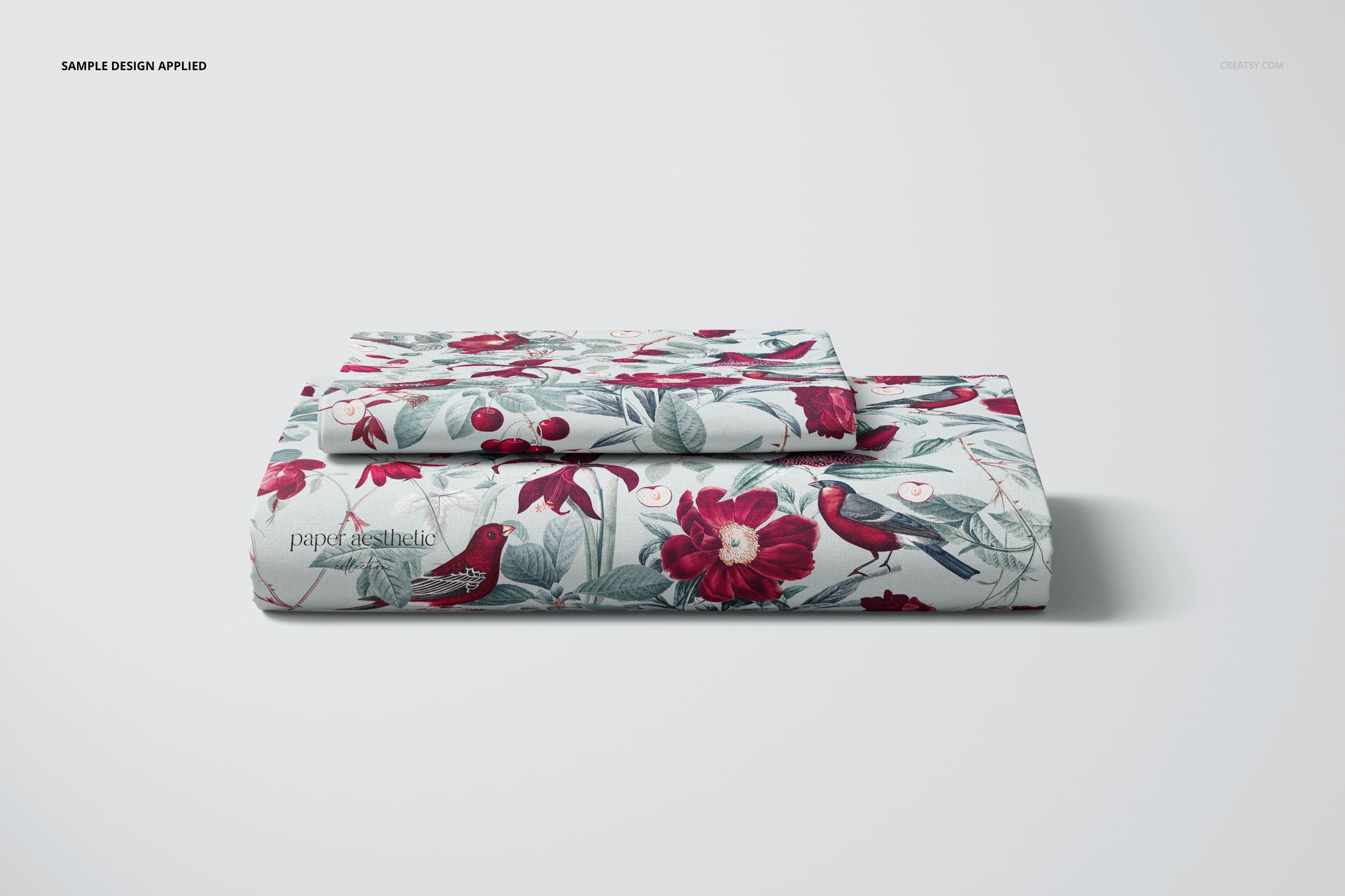 Front view of a folded bed sheet and pillow cover mockup featuring floral and bird motifs in red and green colors.