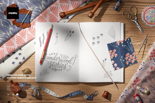 Top view of a creative desk featuring cotton fabric samples with floral patterns, open sketchbook, pencils, and sewing tools.