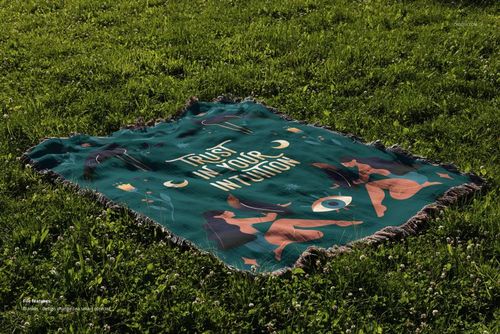 Mockup of a woven throw blanket with fringed edges, featuring colorful art and text, displayed on a grassy lawn.