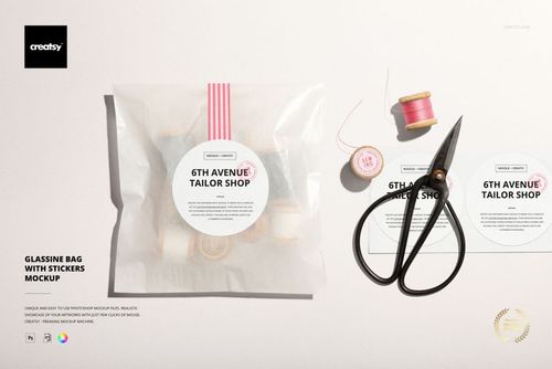 Mockup scene featuring a glassine packaging bag with a sticker label, scissors, pink thread, and two sticker designs.