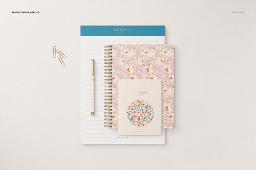 Stationery set mockup featuring a notepad, two floral-patterned planners, a pen, and paper clips on a light surface.