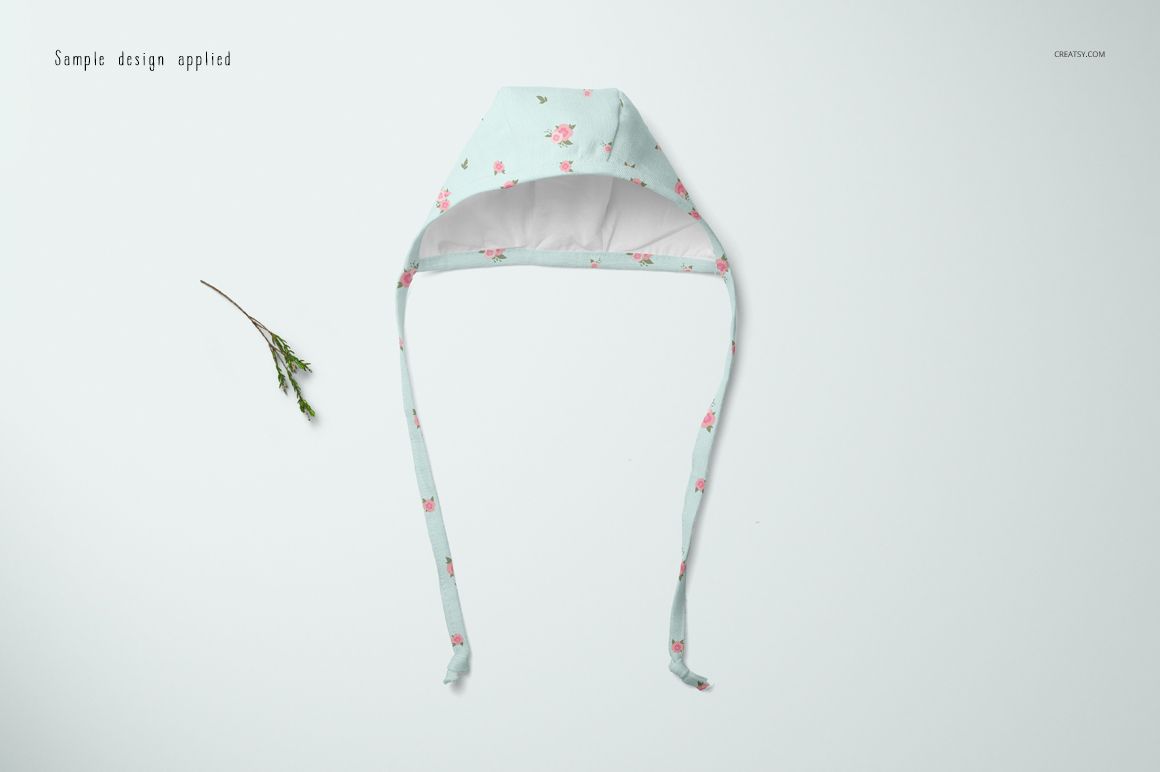 Baby bonnet mockup displayed from top view, light blue fabric with small pink floral pattern and long straps.