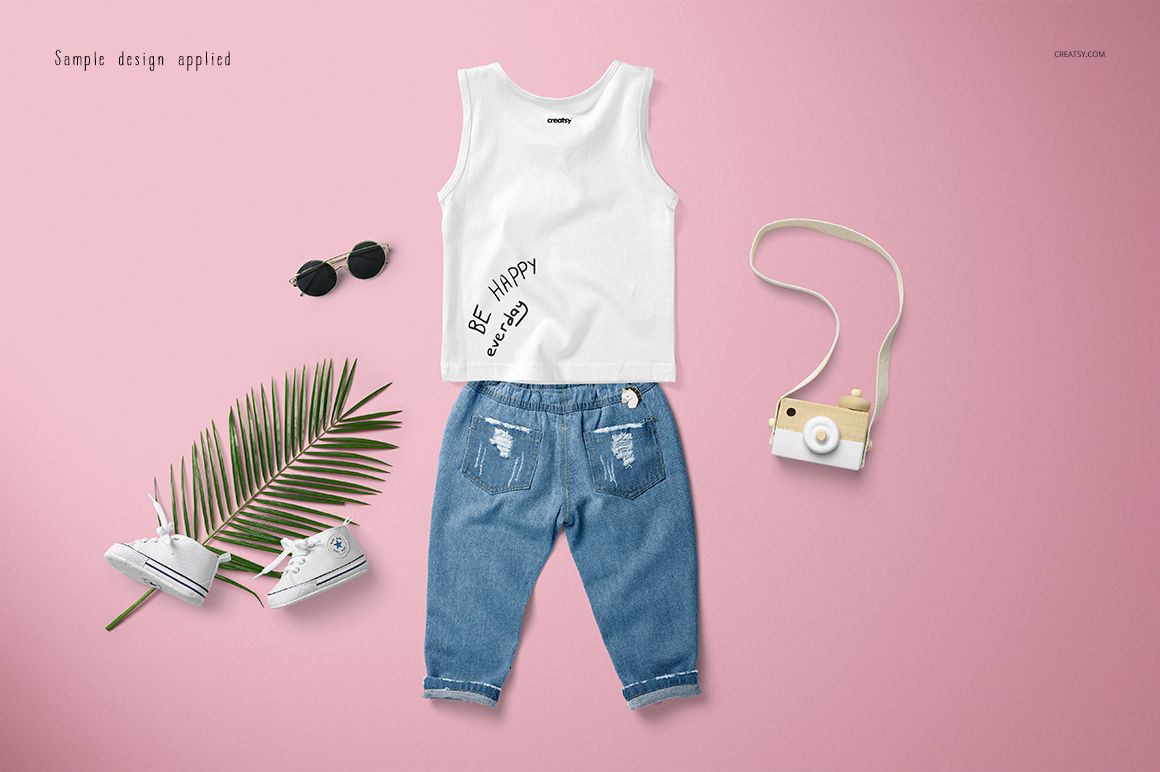 Front view of a baby tank top mockup set with blue jeans, white shoes, sunglasses, and a toy camera on a pink surface.