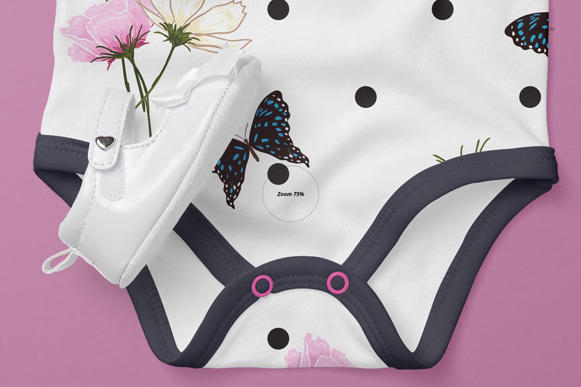 Close-up of a baby onesie mockup with black polka dots, butterfly and floral patterns, dark trim, and a white baby shoe on a pink surface.