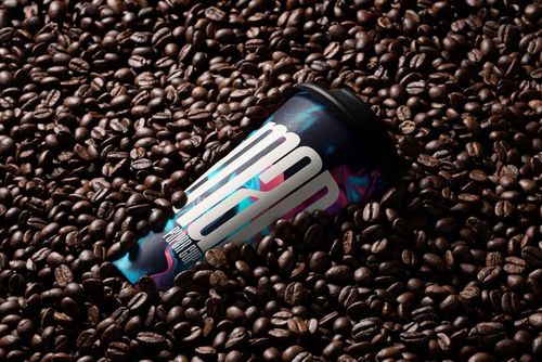 PSD mockup of a paper cup with vibrant patterns, partially buried in a pile of dark roasted coffee beans.