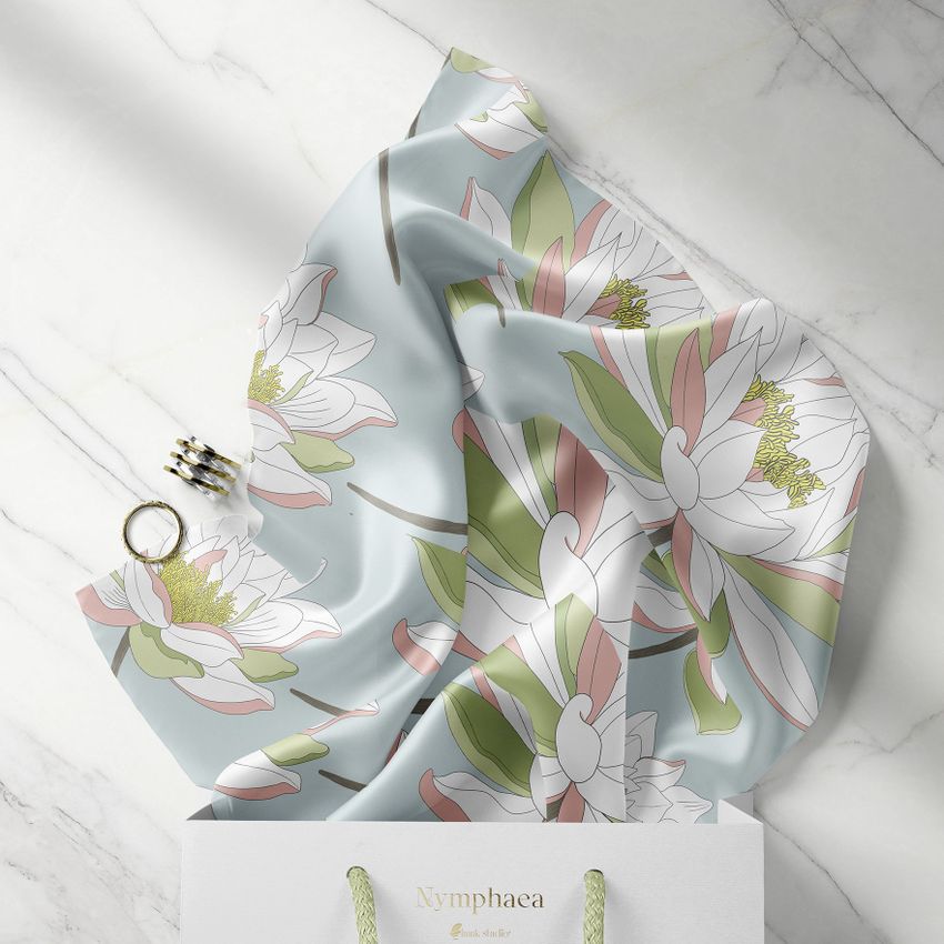Silk scarf mockup with a pastel floral pattern draped on a marble surface, partially placed inside a white shopping bag.