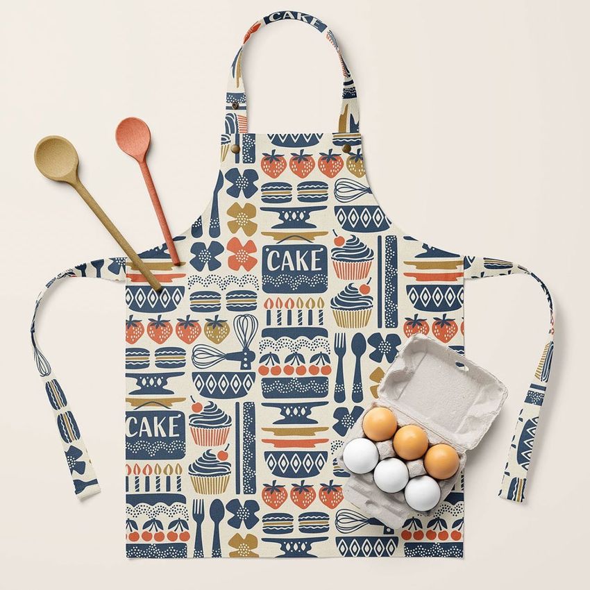 Kids apron mockup featuring a colorful Scandinavian-inspired pattern with cakes, utensils, and eggs on a light surface.