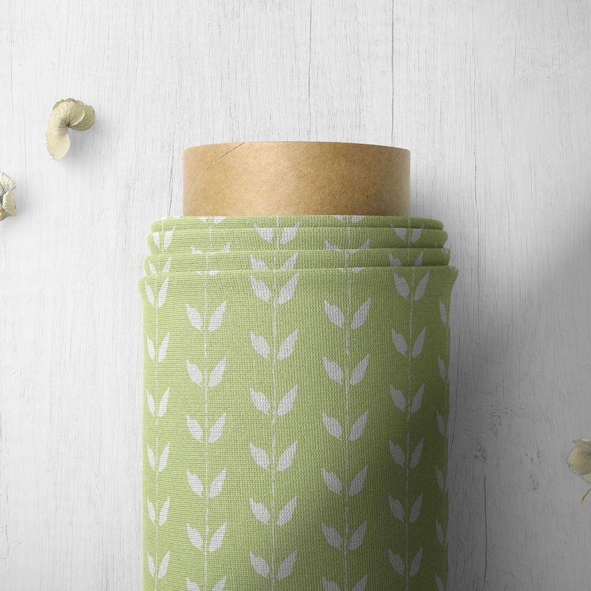 Top view closeup of a fabric roll mockup featuring light green fabric with a white leaf pattern on a light wooden surface.