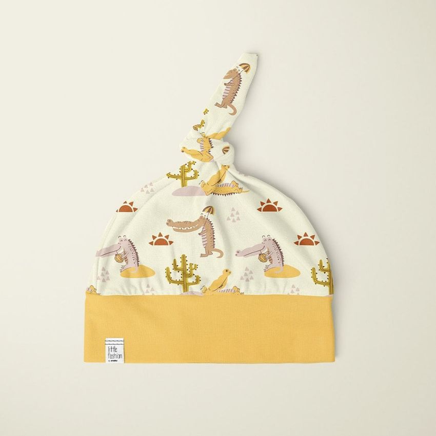 Swaddle set mockup featuring a baby hat with a knotted top, decorated with crocodile and cactus patterns on a cream background.