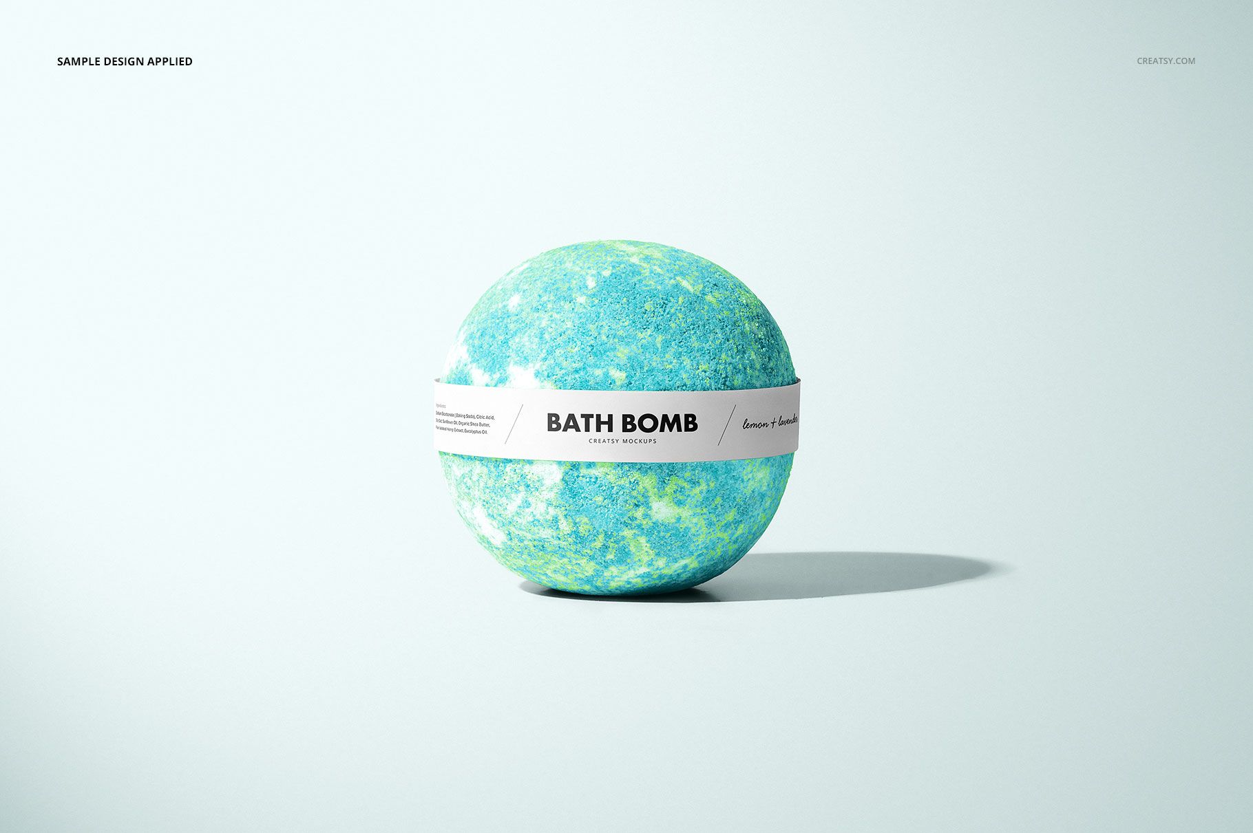 Bath bomb mockup with a white paper band, viewed from the front, showing marbled colors and minimal scene props.