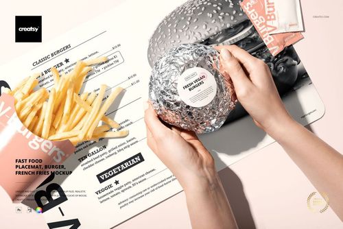 Fast food PSD mockup showing a burger in foil, French fries, and a placemat with a menu design, viewed from above.
