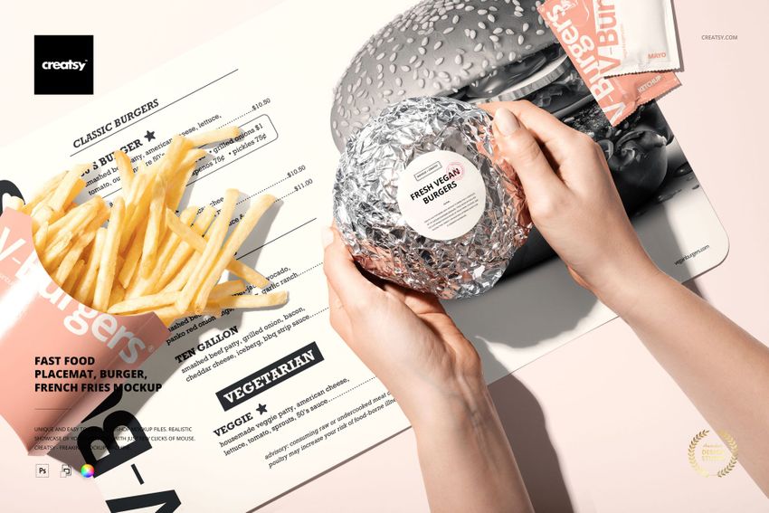 Fast food PSD mockup showing a burger in foil, French fries, and a placemat with a menu design, viewed from above.