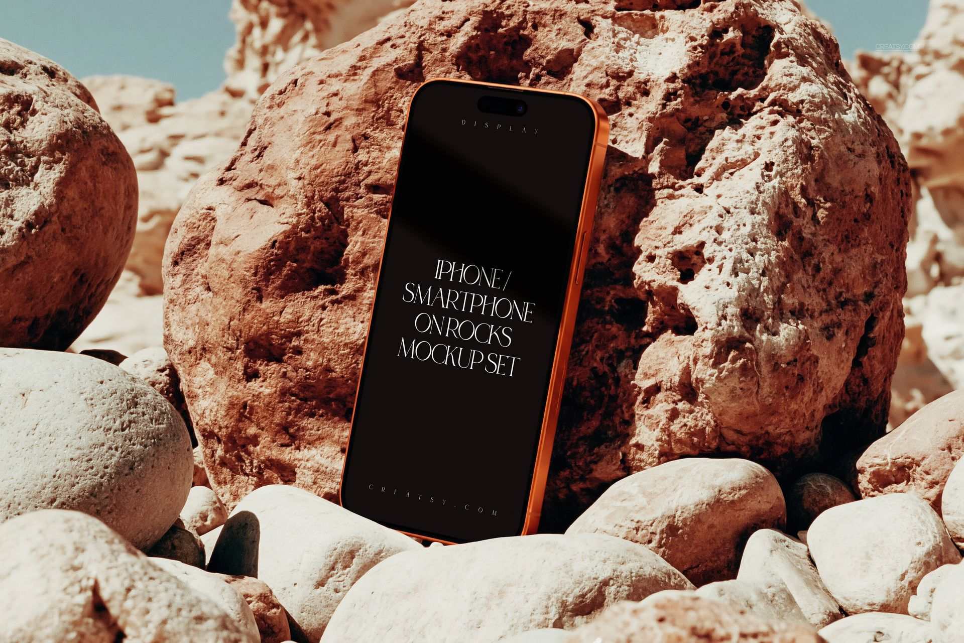 PSD mockup of an iPhone smartphone positioned vertically on rocky terrain, screen facing forward.