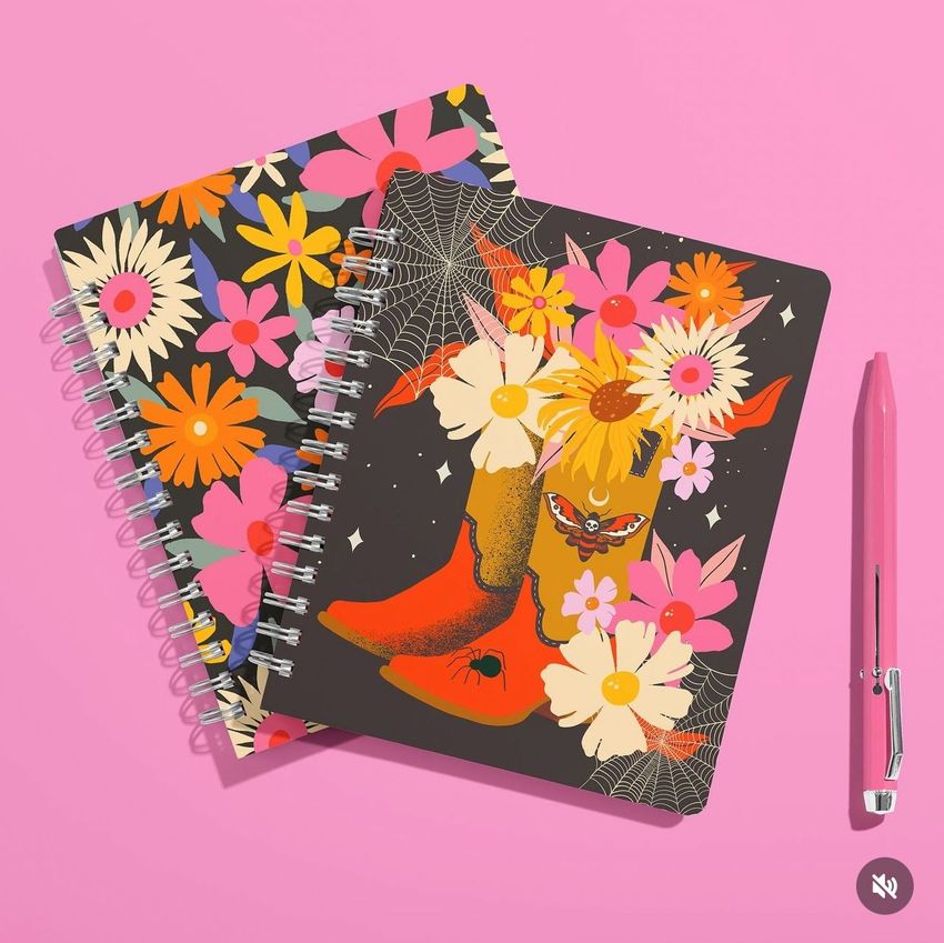 Coiled notebook mockup featuring two spiral-bound notebooks with colorful floral covers, placed on a pink background beside a pink pen.