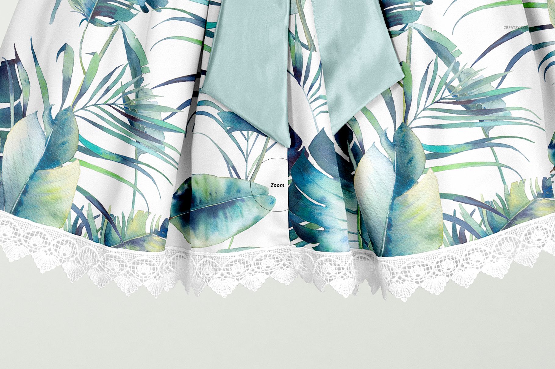 Close-up front view of a kids dress mockup with a green bow, tropical leaf pattern, and white lace trim.