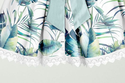 Close-up front view of a kids dress mockup with a green bow, tropical leaf pattern, and white lace trim.