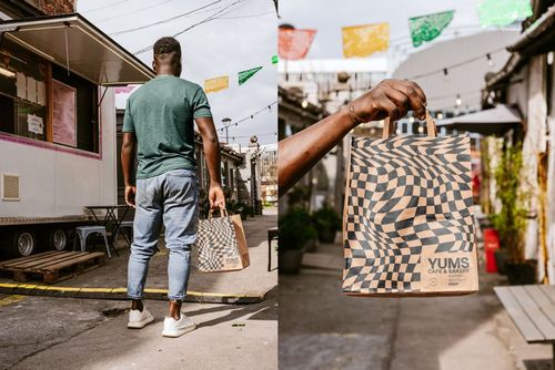 PSD mockup of a patterned paper bag being held outdoors, with colorful flags and urban surroundings in the background.