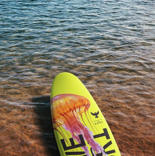 Yellow surfboard longboard mockup featuring a colorful jellyfish illustration, shown from a top view in clear water.