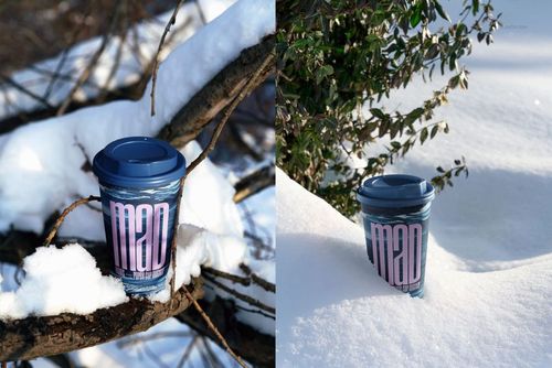 Winter-themed paper cup mockup featuring a blue lid and graphic print, displayed on snowy branches and snowbank.