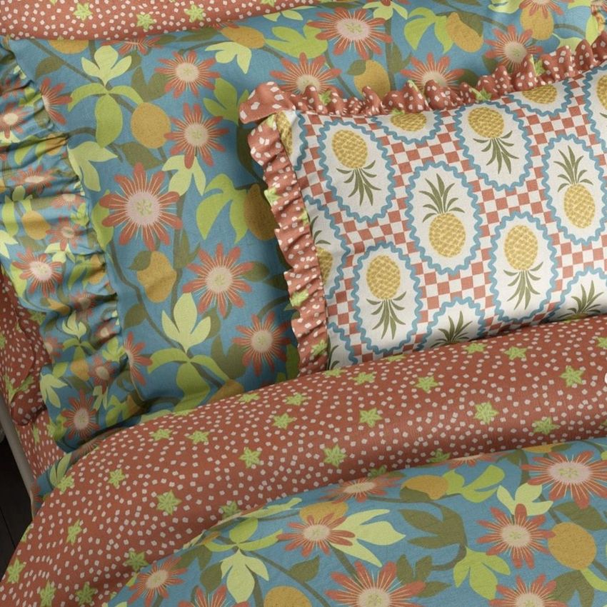 Ruffled pillows and duvet cover mockup featuring tropical fruit and floral patterns in orange, blue, green, and yellow tones.