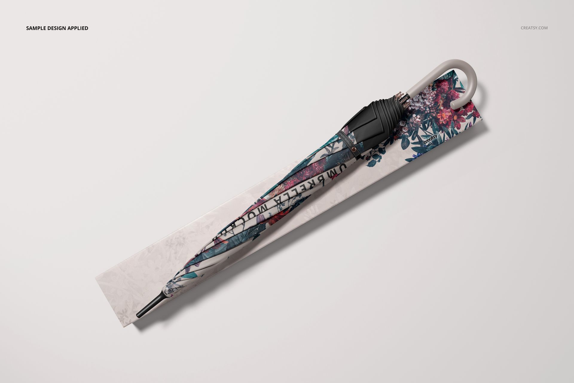 Top-down view of umbrella packaging mockup with floral design, handle and tip visible, set on a plain backdrop.