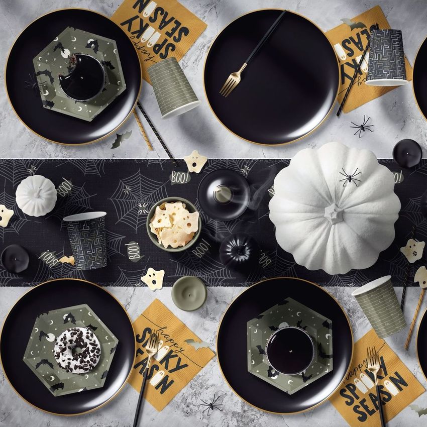 Halloween table setup mockup featuring black plates, gold cutlery, patterned napkins, and decorative pumpkins on a spiderweb table runner.