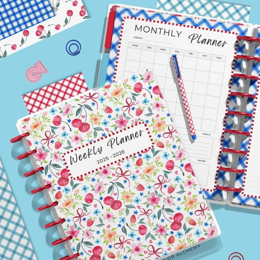 Top view of two spiral planners on a blue surface, one with a cherry and floral cover, the other open to a monthly planner page.