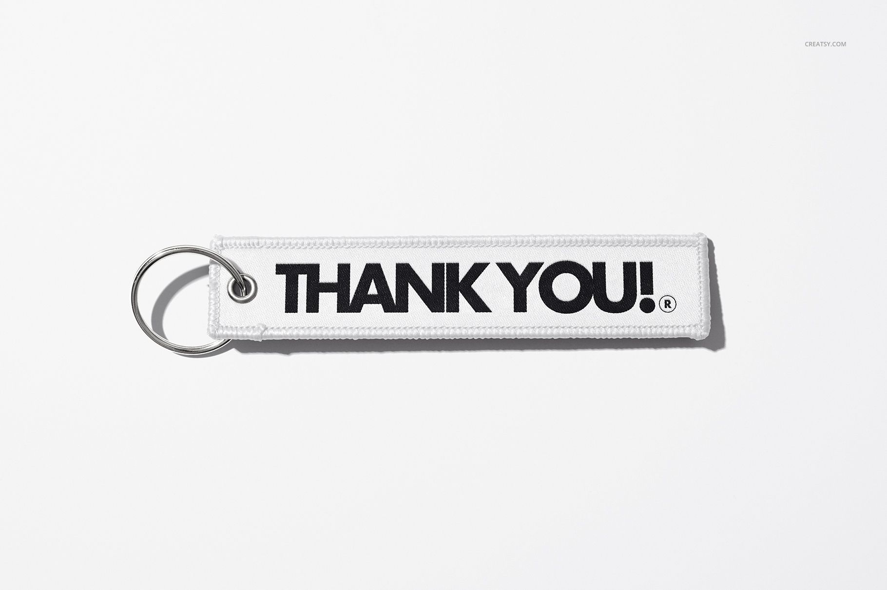 White fabric keychain mockup featuring large black lettering, metal ring attached, displayed on a plain white surface.