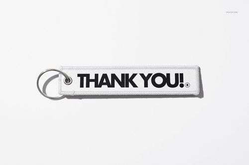 White fabric keychain mockup featuring large black lettering, metal ring attached, displayed on a plain white surface.