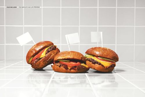 Front view of a burger trio mockup with blank white flags, arranged on a glossy white tile background.
