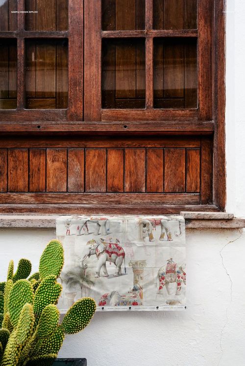PSD mockup of printed fabric with elephants and columns, positioned on a rustic windowsill beside a cactus plant.