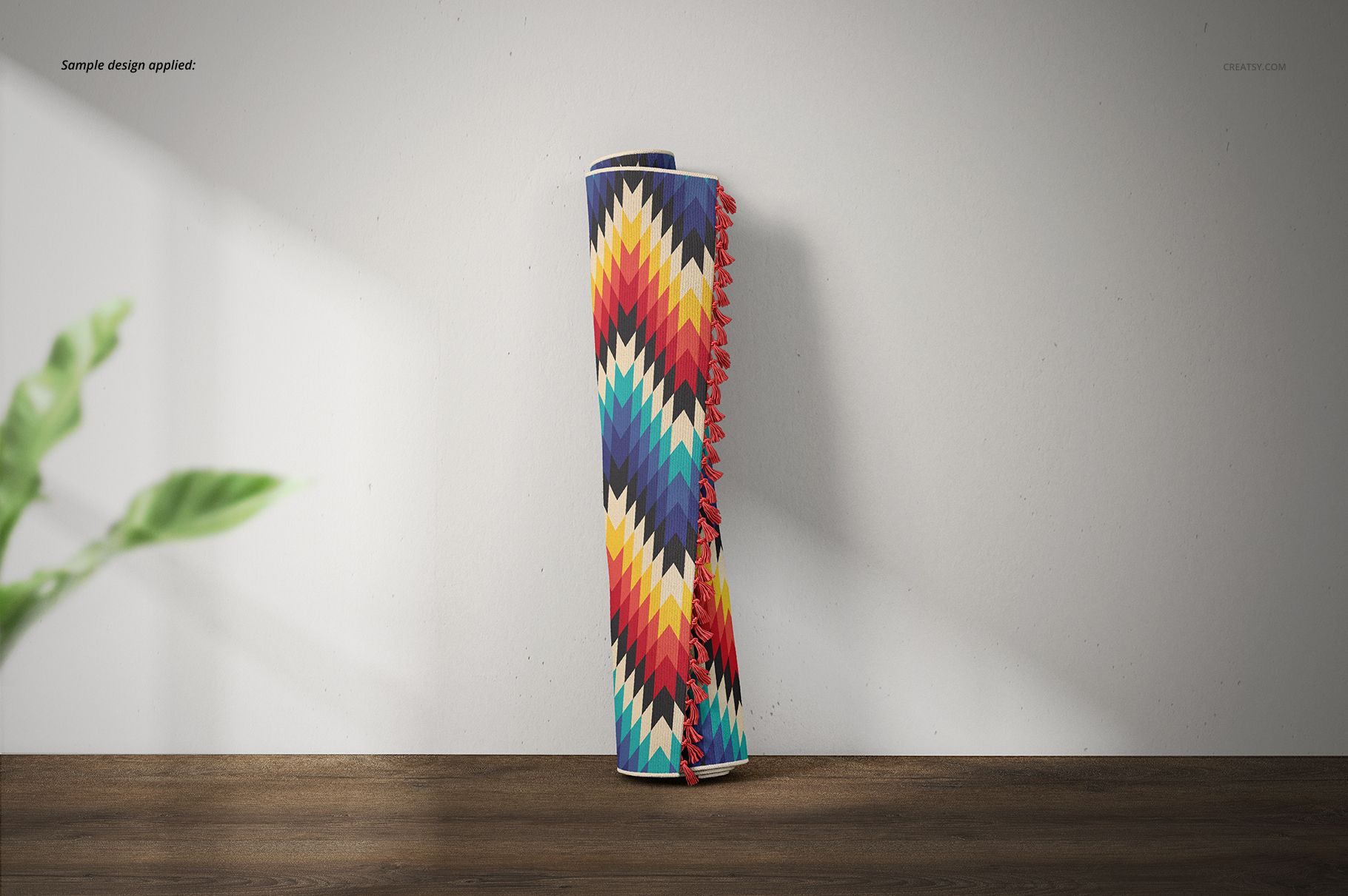 Colorful fringed rug mockup featuring a geometric chevron design, upright against a light wall with plant leaves nearby.