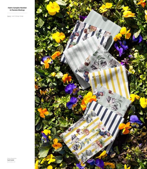 PSD mockup of patterned fabric pieces laid out on a bed of grass, surrounded by yellow and purple blossoms in sunlight.