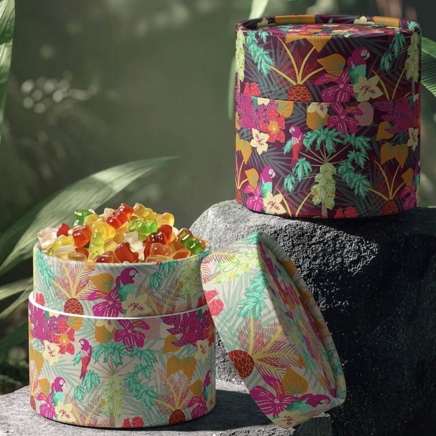 Paper tube packaging mockup featuring colorful jungle-inspired patterns, filled with assorted gummy candies, set on stone outdoors.