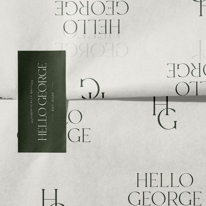 Sticker mockup featuring a rectangular dark green sticker with serif text on folded white paper with repeating logos and text.