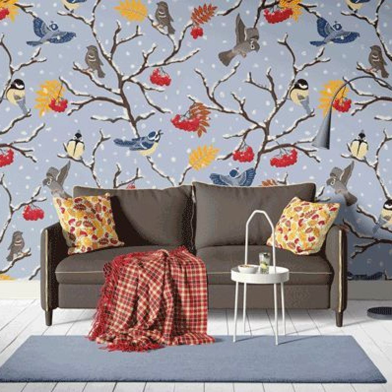 Sofa with pillows wallpaper mockup showing a brown couch in front of a wall with winter branches, birds, and falling snow.