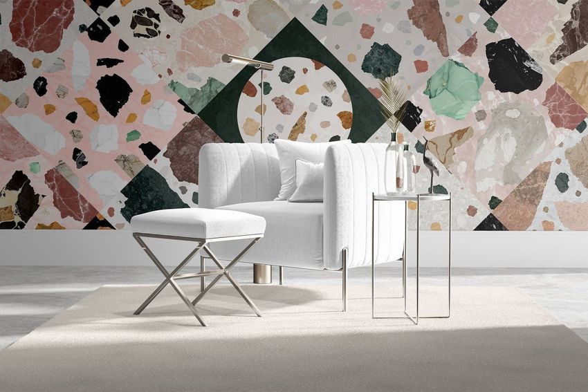 Velvet armchair and stool mockup in a modern interior with a geometric terrazzo-patterned wall, side table, and floor lamp.