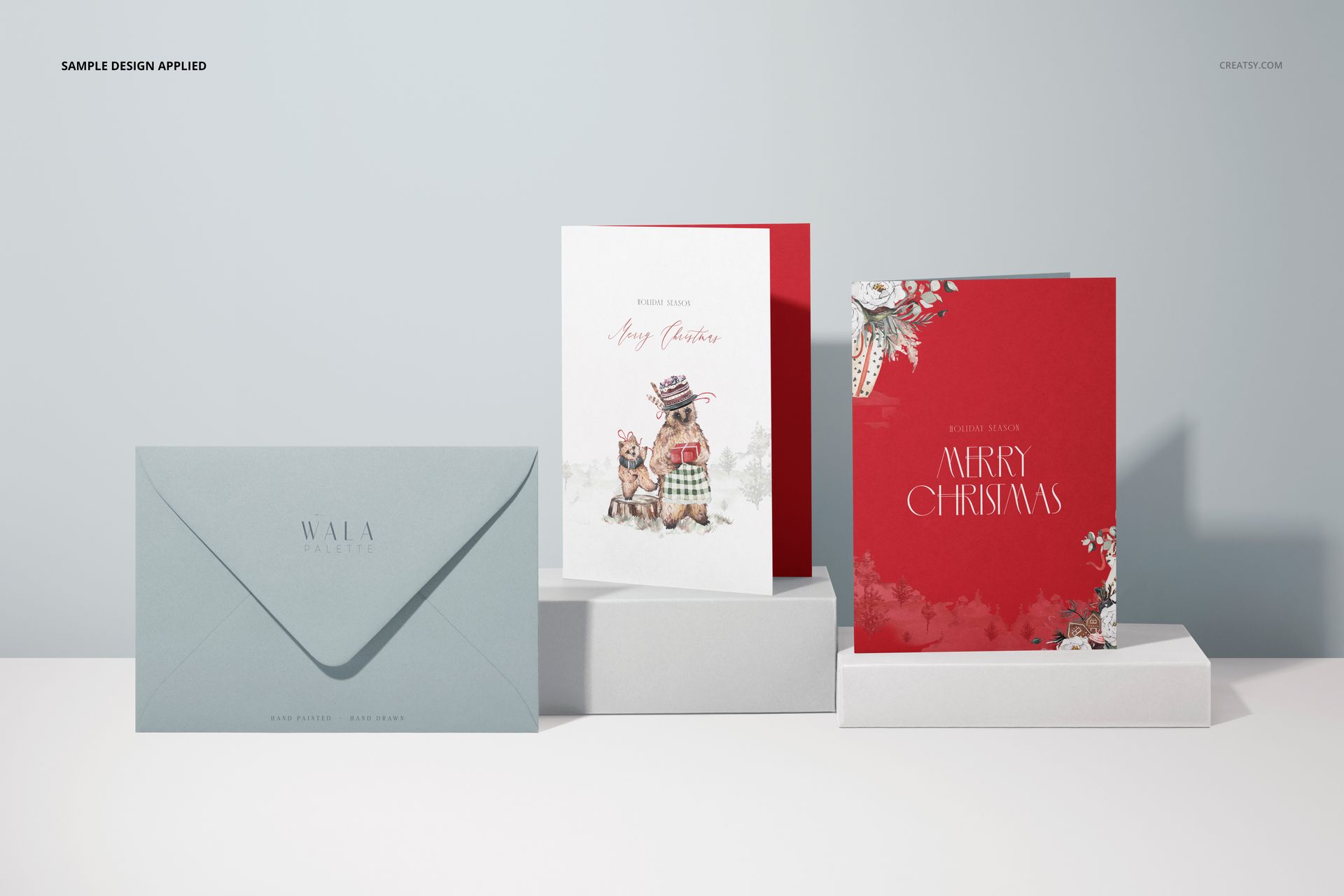 Three 5x7 greeting cards mockup displayed on white platforms, featuring two upright cards and one envelope in soft blue.