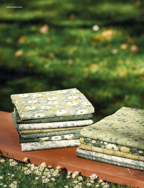 PSD mockup showing multiple fabric pieces with botanical prints stacked on a wooden plank in a meadow scene.