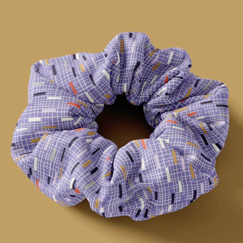 Hair scrunchie mockup featuring a purple fabric with a white grid and colorful stripe pattern on a solid brown background.