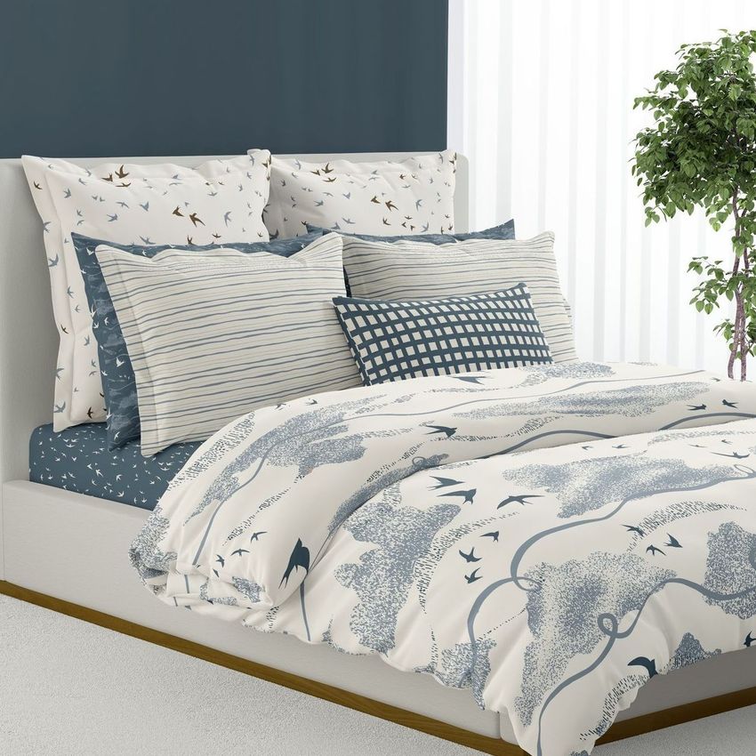 Bedding mockup featuring a bed with patterned duvet cover, multiple pillows with bird and stripe designs, and a potted plant nearby.