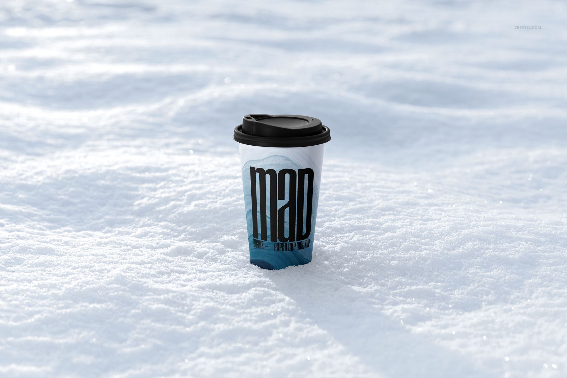Winter-themed paper cup mockup with a black lid and large lettering, placed on textured white snow outdoors.