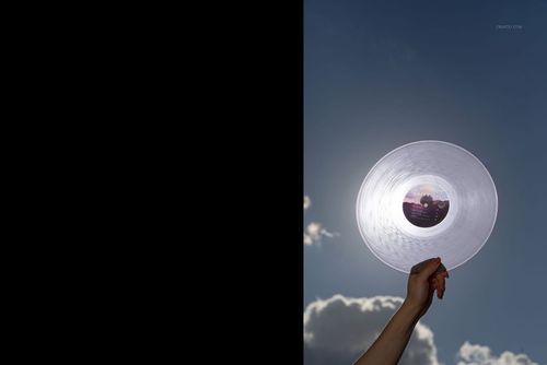Close-up of a clear colored vinyl record mockup held up to the sunlight, with sky and clouds in the background.
