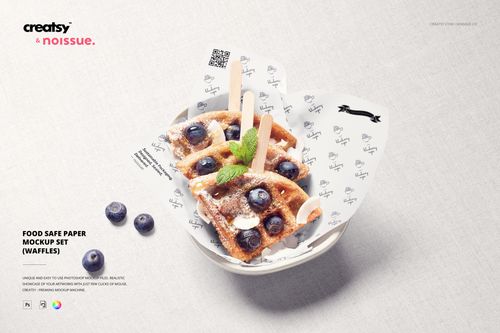 Top view of a bowl with waffles topped with blueberries and mint, wrapped in patterned food safe paper mockup on a light surface.
