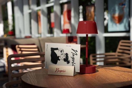Front view of a restaurant menu mockup displayed on a round wooden table with a red lamp and sunlit background.
