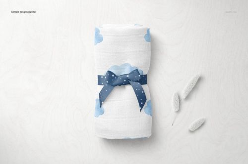 PSD mockup showing a folded baby muslin nappy with cloud design and ribbon, styled on a light tabletop with props.