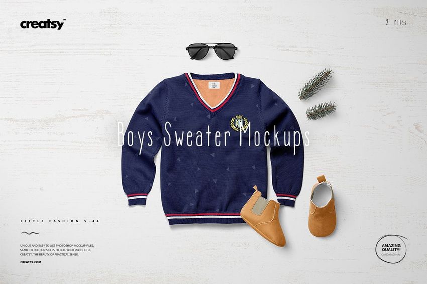 Front view of a boys sweater mockup in navy blue with red and white trim, styled with shoes, sunglasses, and pine branches.