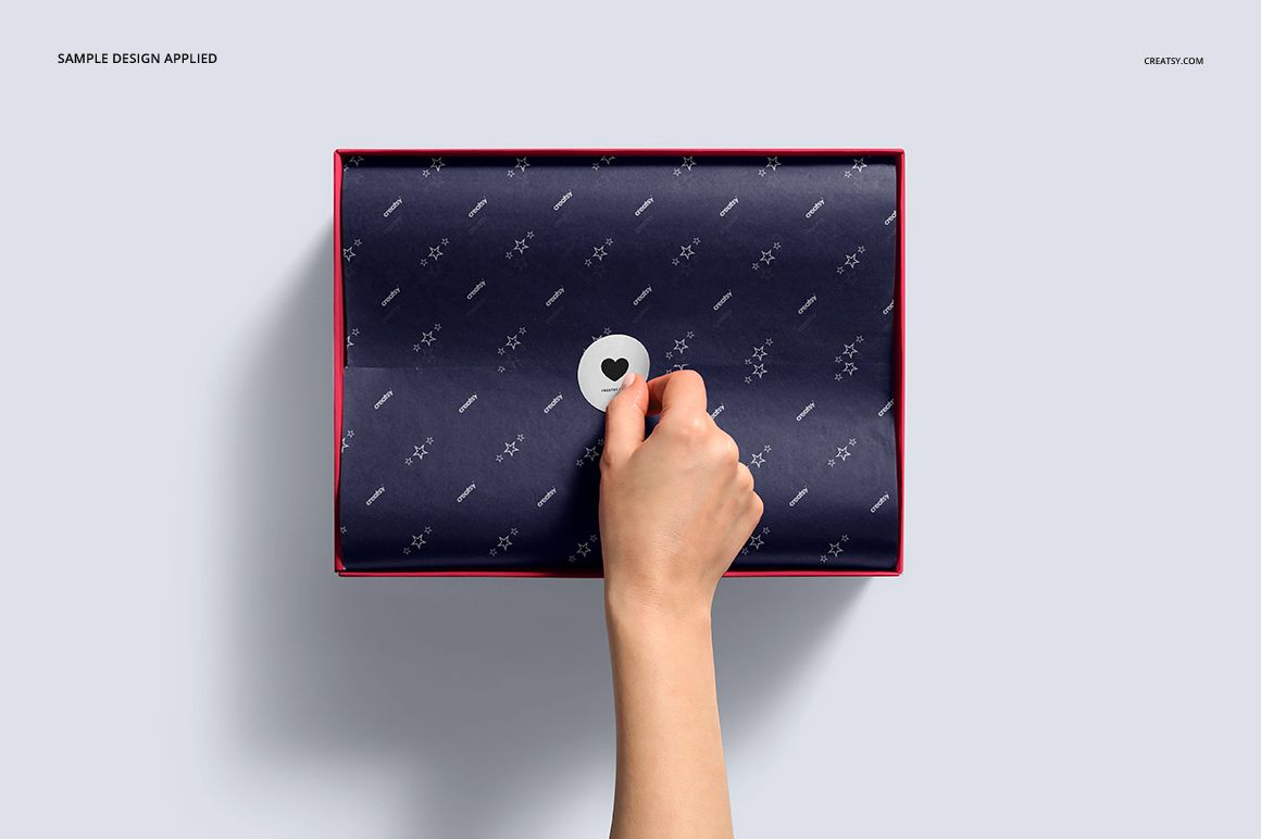 PSD mockup showing a shoe box with a navy blue patterned lid, heart-shaped sticker, and hand opening the box.
