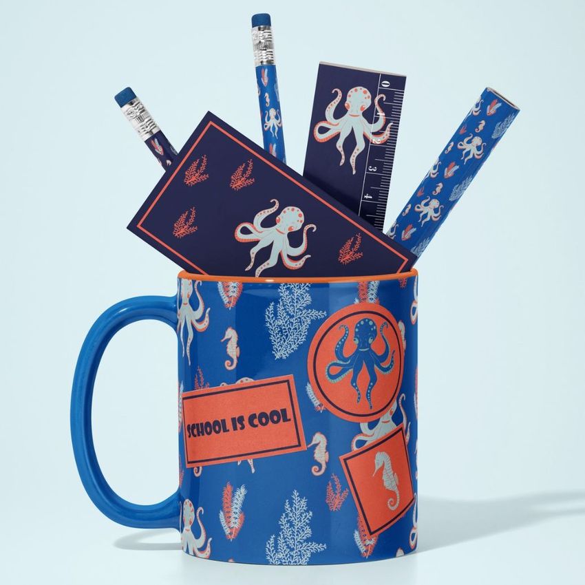 Mug mockup featuring a blue mug with sea creature patterns, filled with matching pencils, a ruler, and cards on a light background.